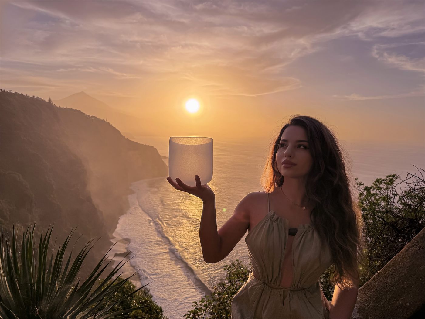 Xenia holding a crystal bowl at sunset, above the ocean